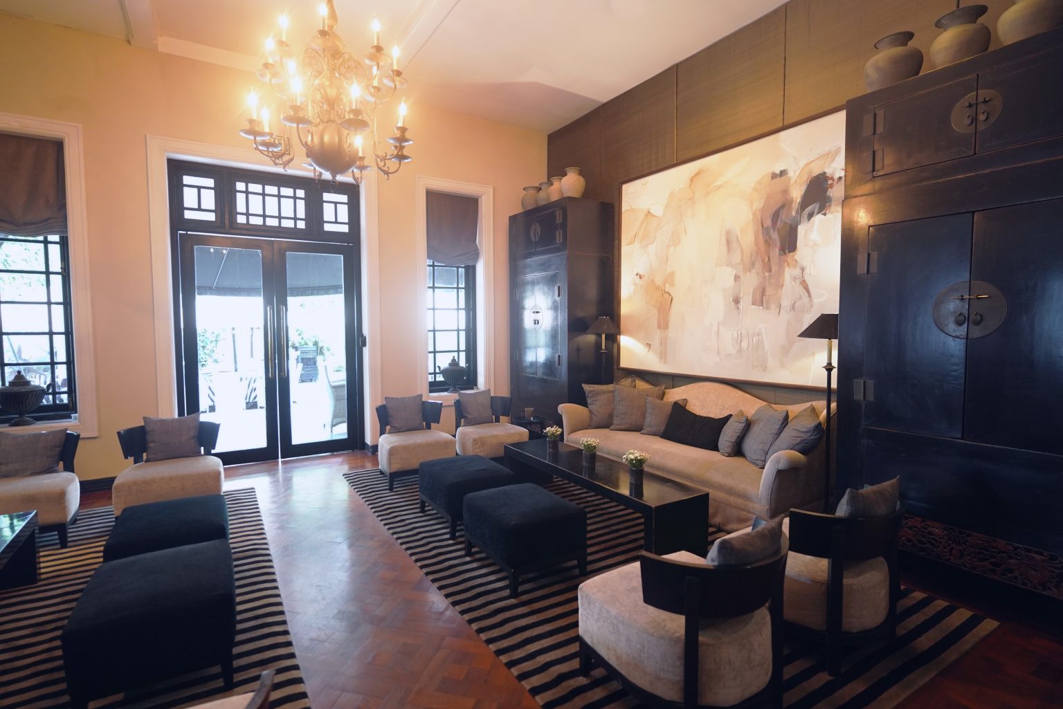 A high-ceilinged lounge with a chandelier, a large abstract painting and French doors
