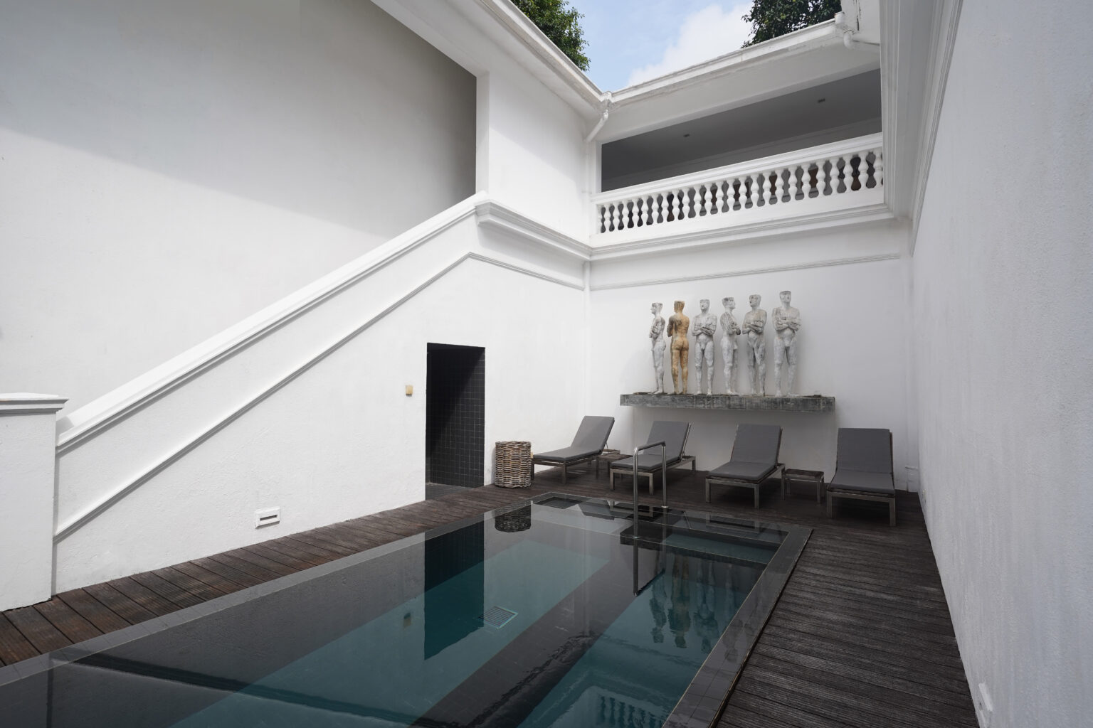 The lap pool in a white-walled courtyard, with loungers and a row of sculpted figures